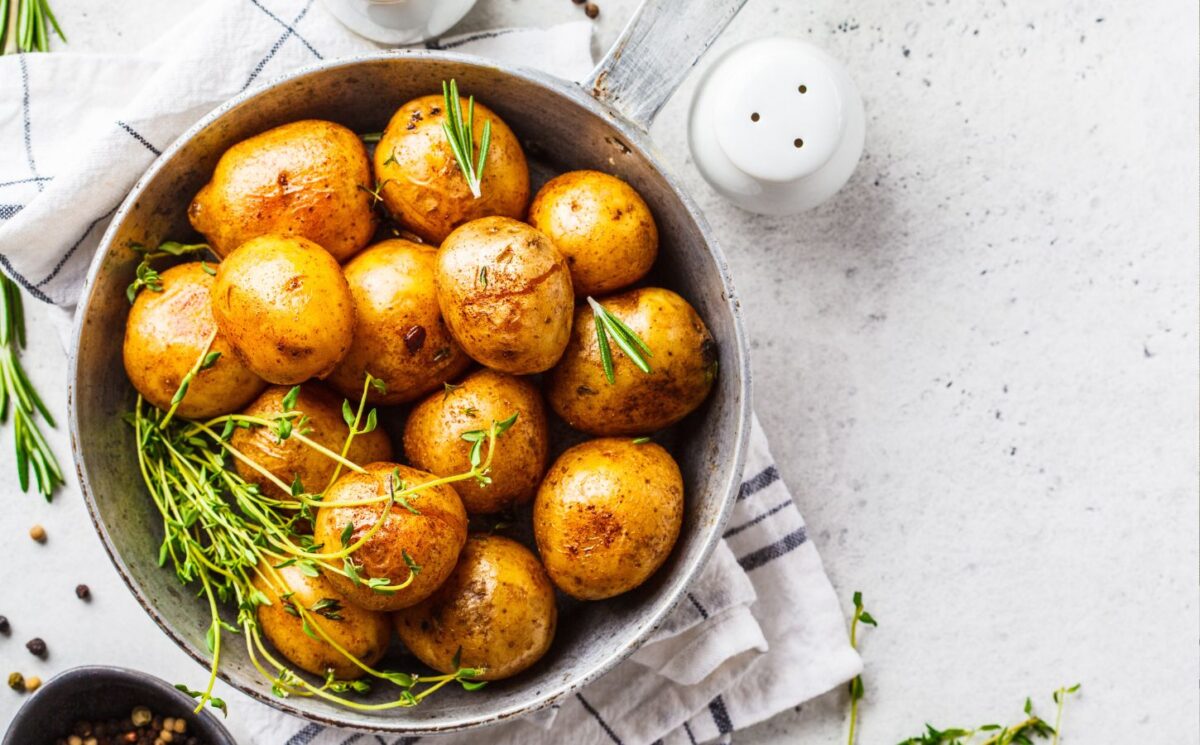 Baked potatoes in a bowl sprinkled with green herbs, illustrating the health benefits of white potatoes