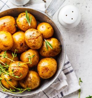 Baked potatoes in a bowl sprinkled with green herbs, illustrating the health benefits of white potatoes