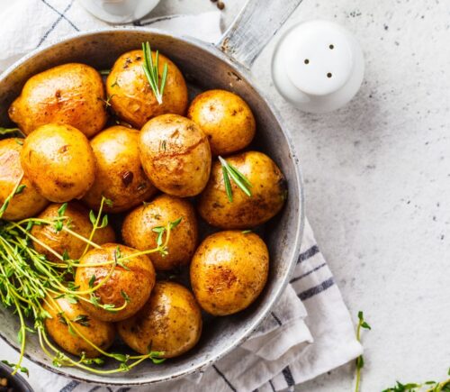 Baked potatoes in a bowl sprinkled with green herbs, illustrating the health benefits of white potatoes
