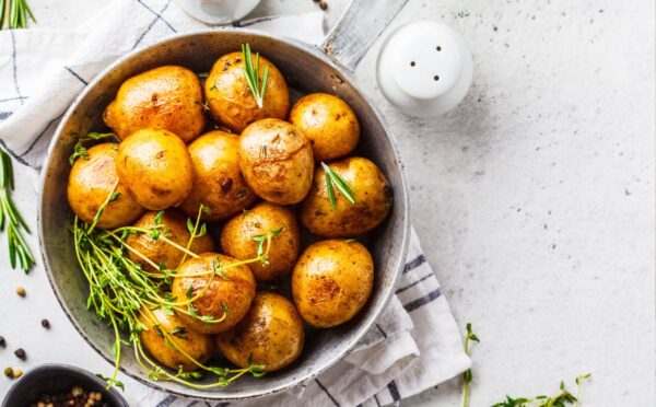 Baked potatoes in a bowl sprinkled with green herbs, illustrating the health benefits of white potatoes