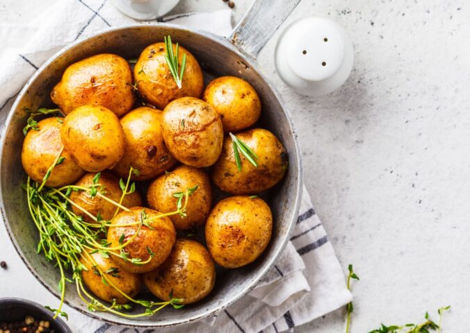 Baked potatoes in a bowl sprinkled with green herbs, illustrating the health benefits of white potatoes