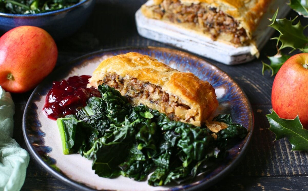 a slice of apple, parsnip and mushroom wellington with onion, garlic, and green lentils with a side of greens