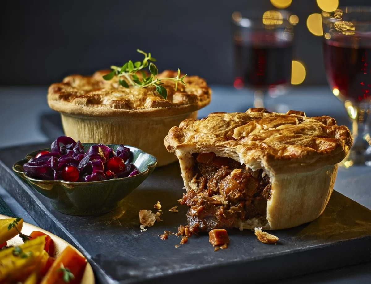 Photo shows the Tesco Finest No-Beef Bourguignon Pie with cranberry sauce and glasses of red wine