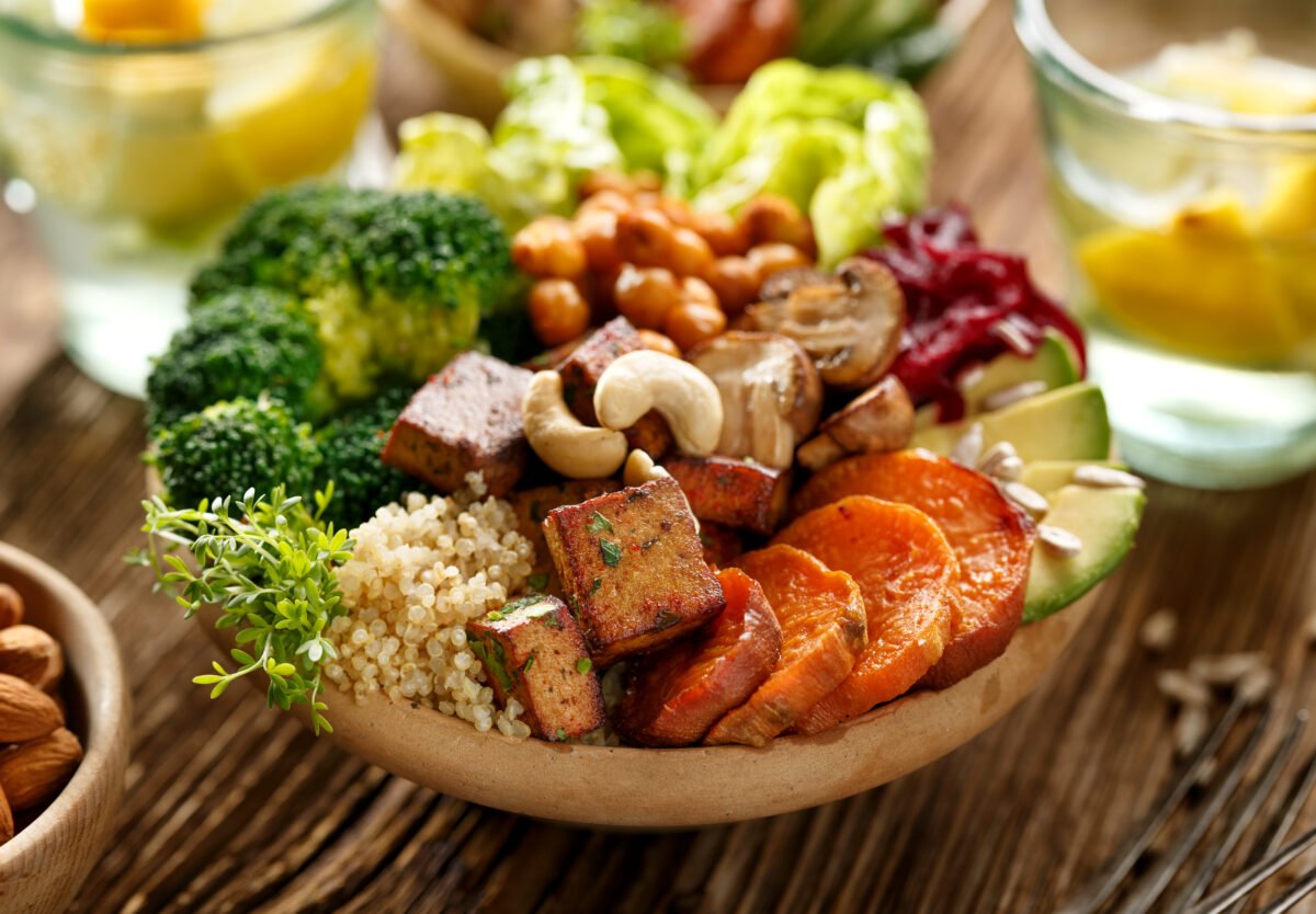 Photo shows a large, nutritionally balanced bowl of plant-based food including tofu, nuts, vegetables, and grain