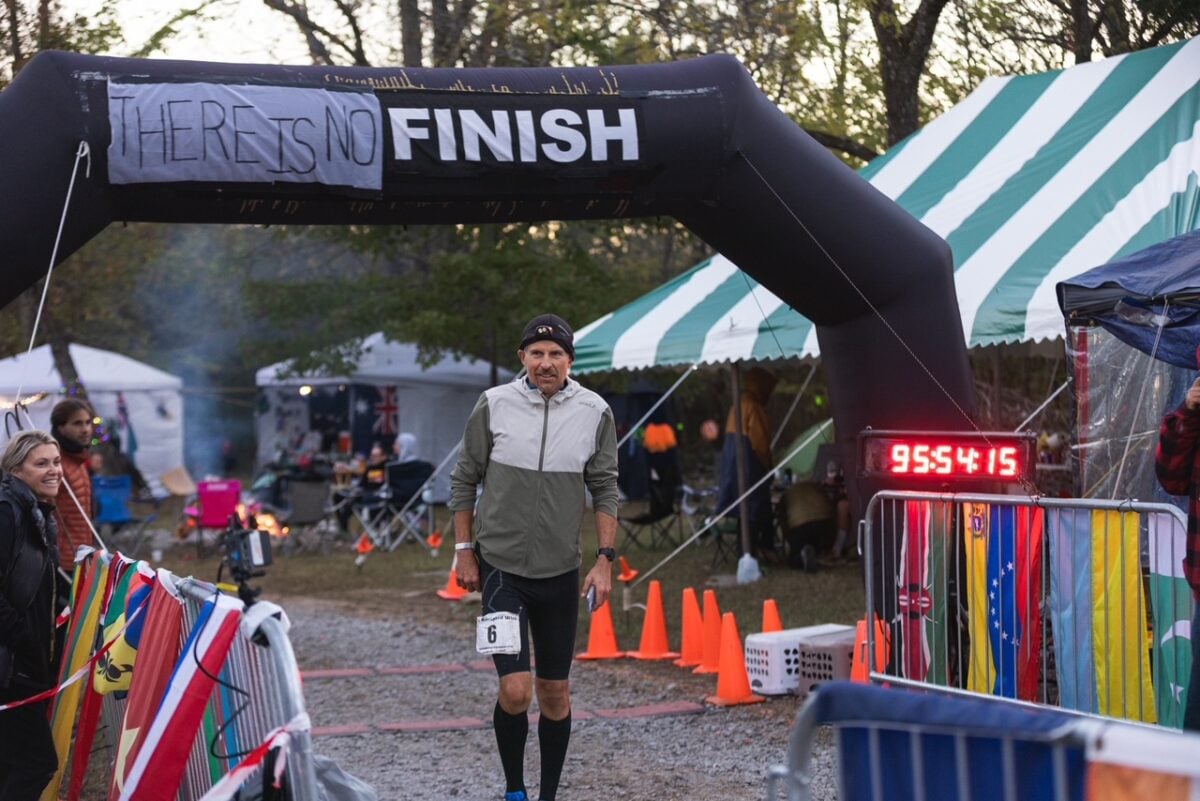 Photo shows vegan runner Harvey Lewis standing at the altered finish line for Big Dog's Backyard Ultra, which reads "there is no finish"
