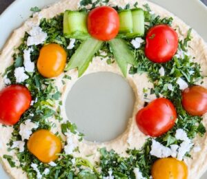 a vegan hummus Christmas wreath with parsley, cherry tomatoes, and cucumber