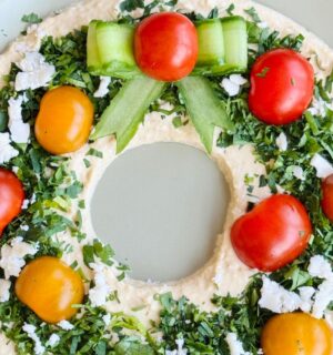 a vegan hummus Christmas wreath with parsley, cherry tomatoes, and cucumber