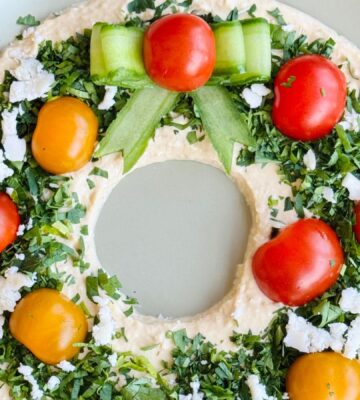 a vegan hummus Christmas wreath with parsley, cherry tomatoes, and cucumber