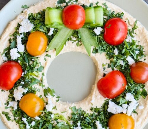 a vegan hummus Christmas wreath with parsley, cherry tomatoes, and cucumber