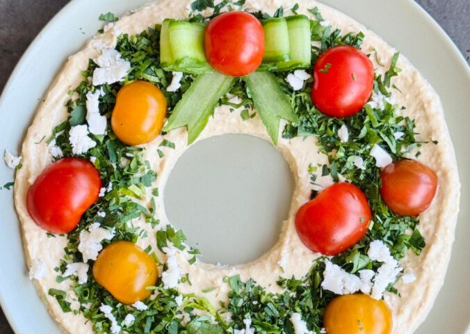 a vegan hummus Christmas wreath with parsley, cherry tomatoes, and cucumber