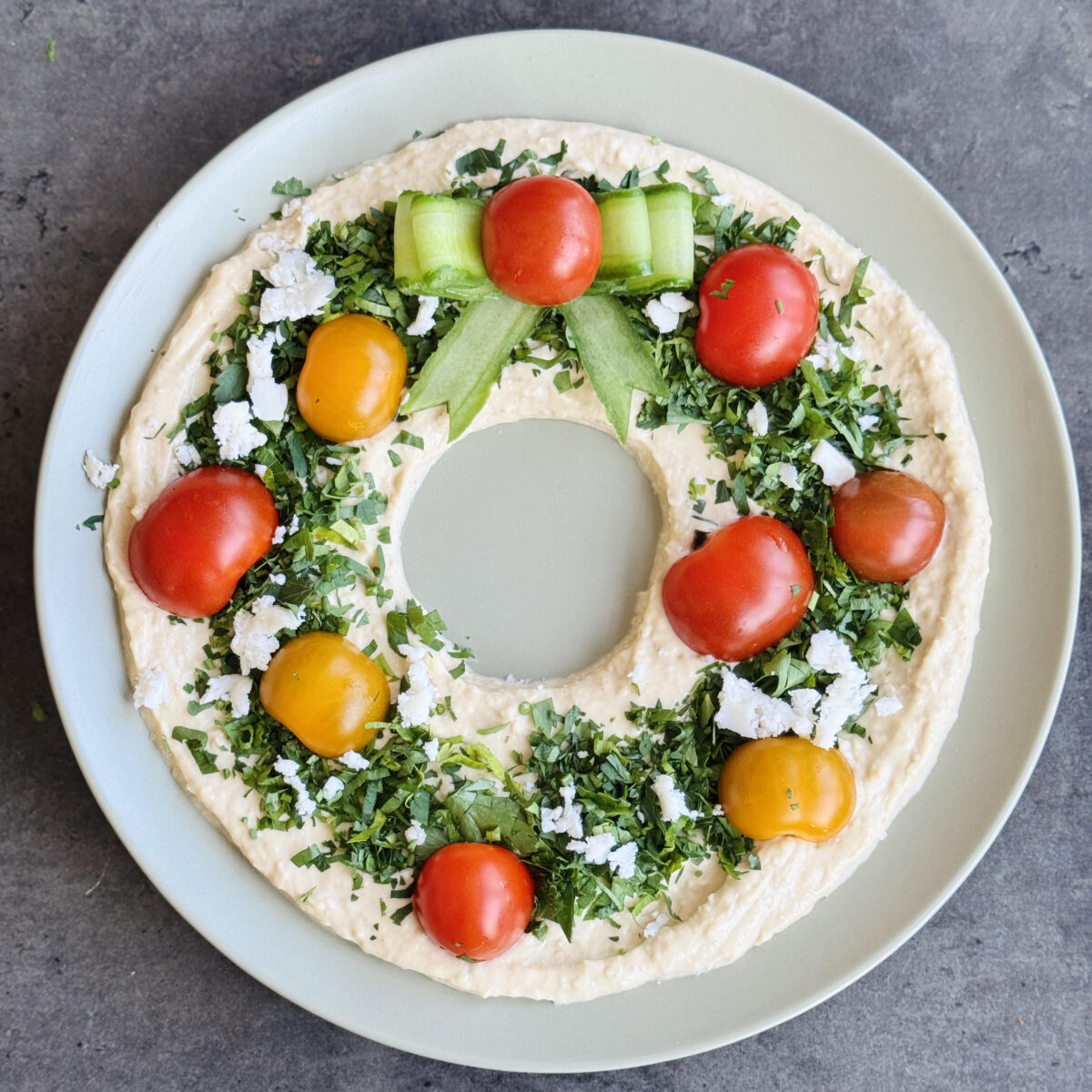a vegan hummus Christmas wreath with parsley, cherry tomatoes, and cucumber