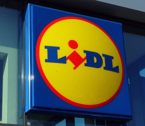 Photo shows the distinctive Lidl sign in red, yellow, and blue above a store entrance. Lidl has called on the UK government to introduce mandatory plant-based sales targets and plant-based sales reporting