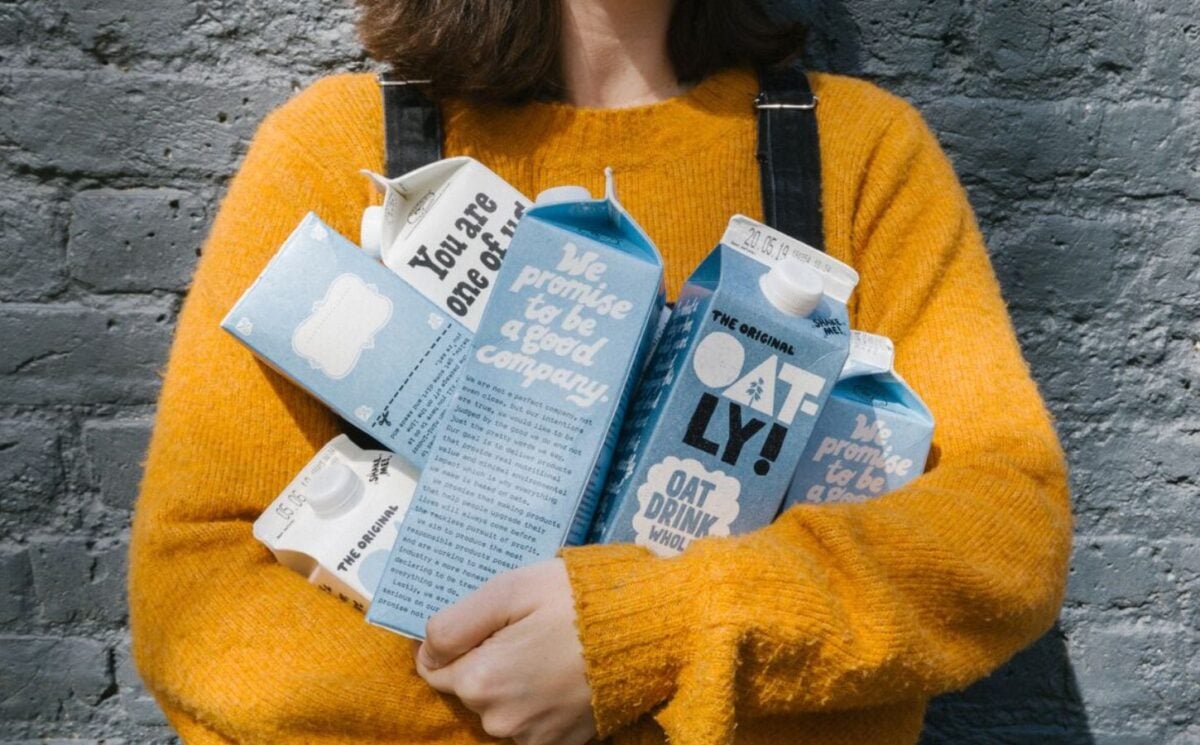 Photo shows a woman in a yellow sweater holding different types of Oatly's oat milk