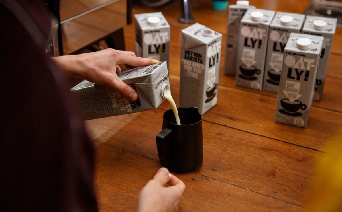 Photo shows someone pouring Oatly's oat milk into a jug for making coffee. Oatly recently announced a profitable growth milestone and a switch to 100 percent British oats