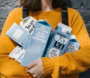 Photo shows a woman in a yellow sweater holding different types of Oatly's oat milk