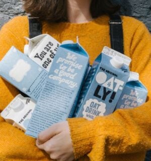 Photo shows a woman in a yellow sweater holding different types of Oatly's oat milk