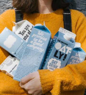 Photo shows a woman in a yellow sweater holding different types of Oatly's oat milk