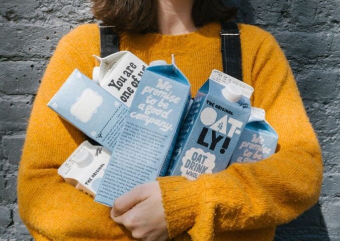 Photo shows a woman in a yellow sweater holding different types of Oatly's oat milk