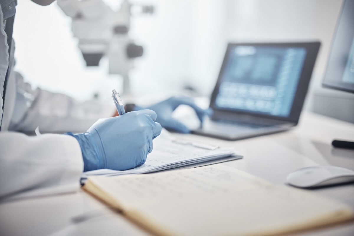 Photo shows someone wearing blue medical gloves in a laboratory setting using a computer