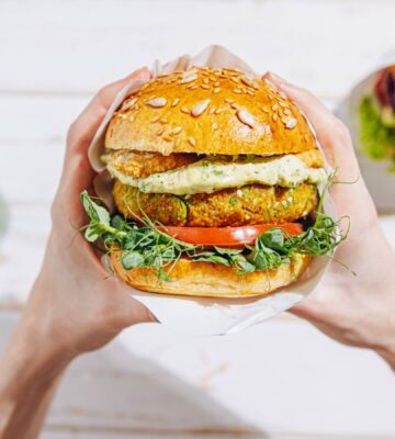 Photo shows a woman's hands holding a large vegetarian burger next to a green smoothie and a second sandwich. A new report suggests that ultra-processed plant-based foods are better for heart health than unprocessed animal foods like meat and dairy