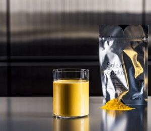 Photo shows a pouch of Solein, a vegan microbial protein by Solar Foods, alongside a small pile of the powdered version and a vibrant yellow drink made of the same