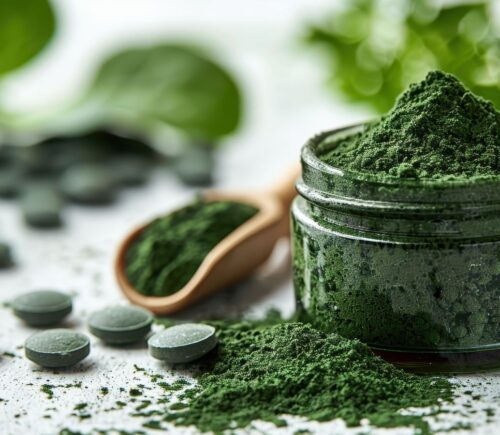 Close-up of green spirulina powder in a jar with tablets and a wooden spoon on a white surface, to showcase the dangers of spirulina