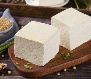 Two blocks of fresh tofu on a wooden cutting board, to illustrate the cancer-protective effects of soy