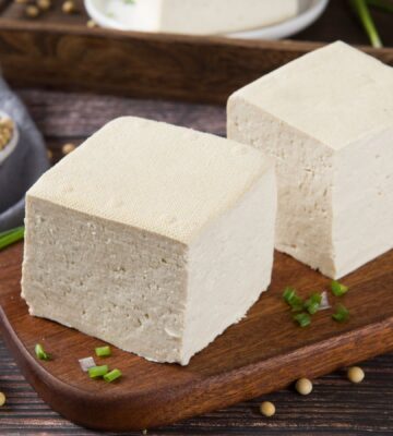 Two blocks of fresh tofu on a wooden cutting board, to illustrate the cancer-protective effects of soy