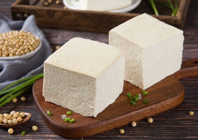 Two blocks of fresh tofu on a wooden cutting board, to illustrate the cancer-protective effects of soy
