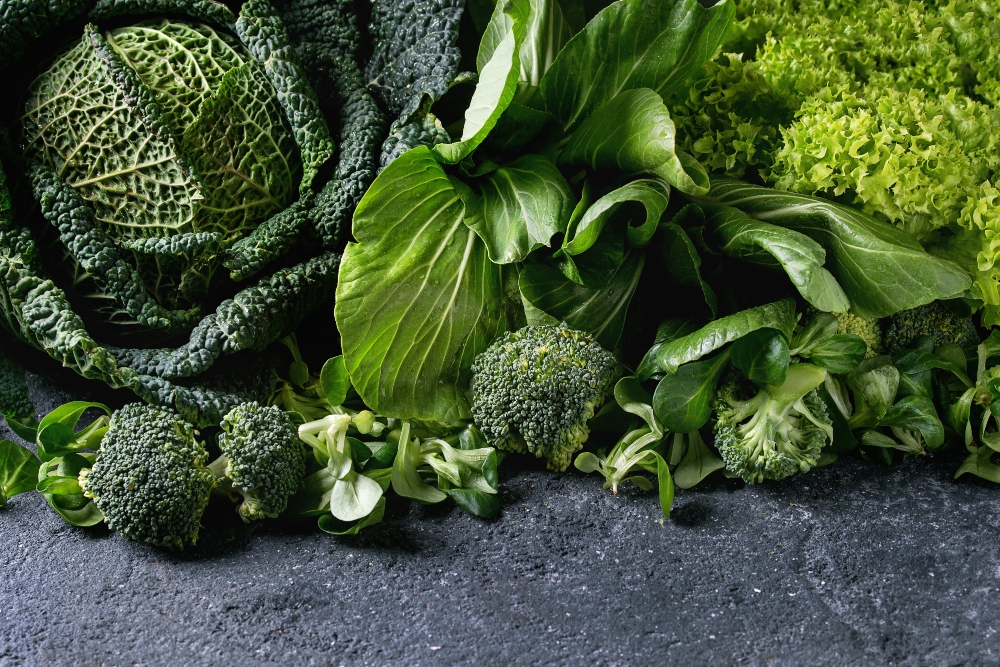 Vitamin A5 is found in leafy greens, such as this variety of raw green vegetables salads, lettuce, bok choy, corn, broccoli, savoy cabbage as frame over black stone texture background