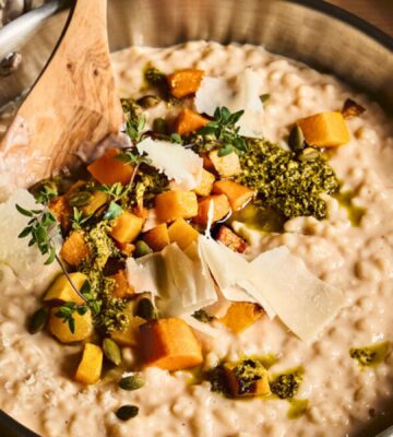 a pan of butternut squash risotto with cognac, pumpkin seed pesto, and fried thyme blossom