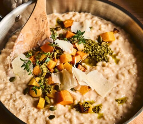 a pan of butternut squash risotto with cognac, pumpkin seed pesto, and fried thyme blossom