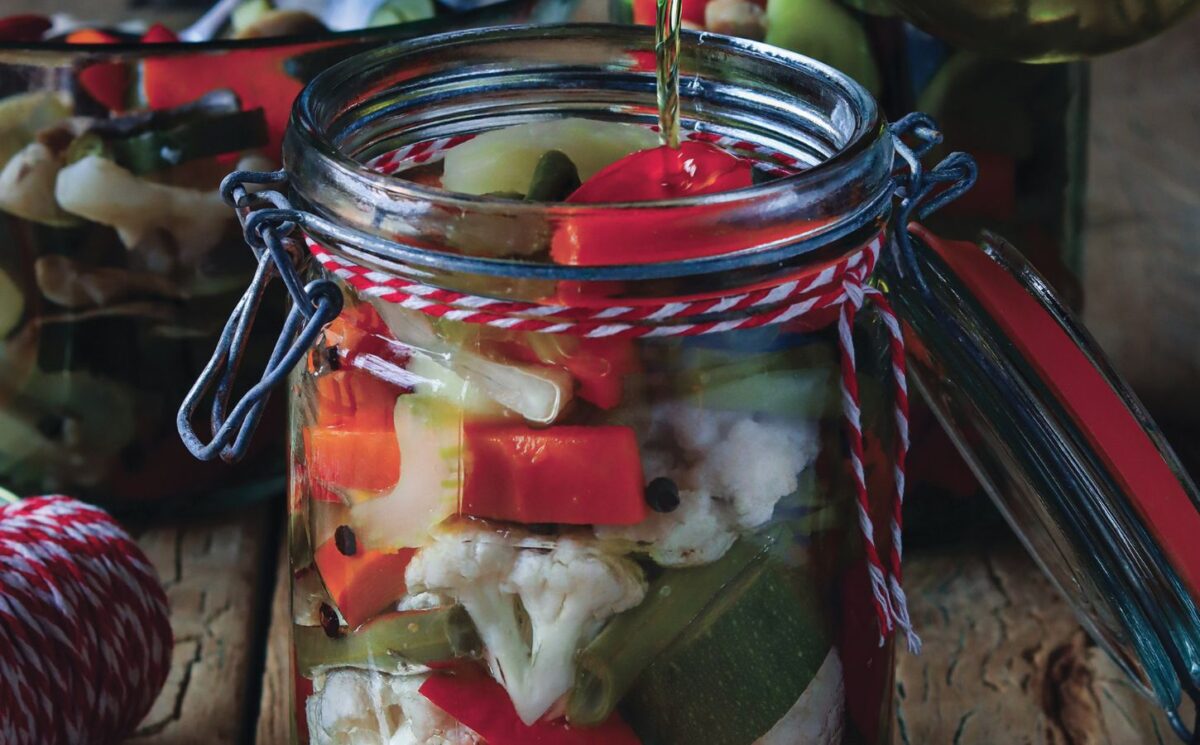 a jar of pickled vegetables with oil including cauliflower, capsicum, and carrots for gluten-free holiday recipes