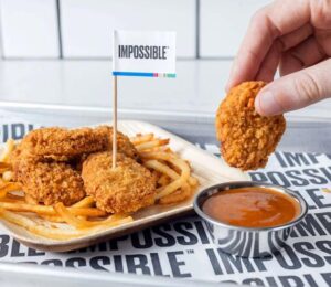 Photo shows someone dunking an Impossible Foods plant-based chicken nugget in a pot of sauce
