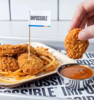 Photo shows someone dunking an Impossible Foods plant-based chicken nugget in a pot of sauce