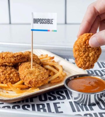Photo shows someone dunking an Impossible Foods plant-based chicken nugget in a pot of sauce