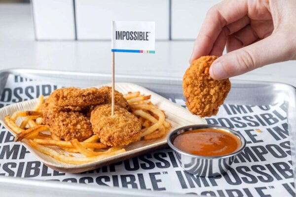 Photo shows someone dunking an Impossible Foods plant-based chicken nugget in a pot of sauce