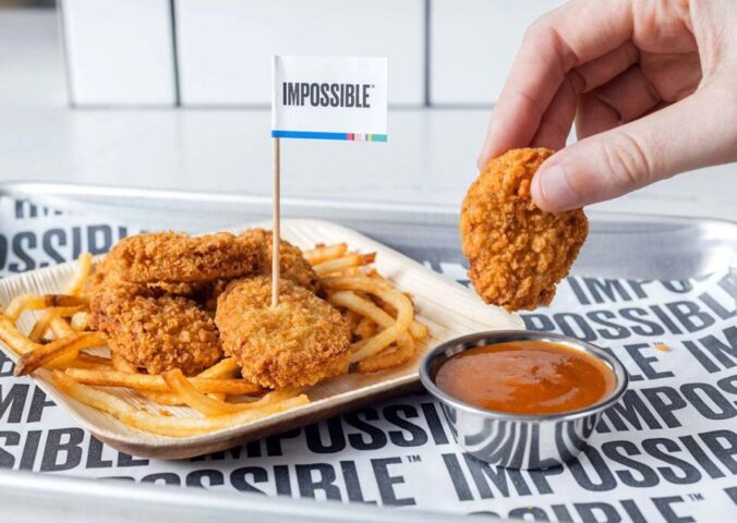 Photo shows someone dunking an Impossible Foods plant-based chicken nugget in a pot of sauce