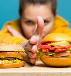 Photo shows a woman holding her hand between two burgers: a traditional beef burger on the left, and a bun filled with sliced fresh fruit on the right