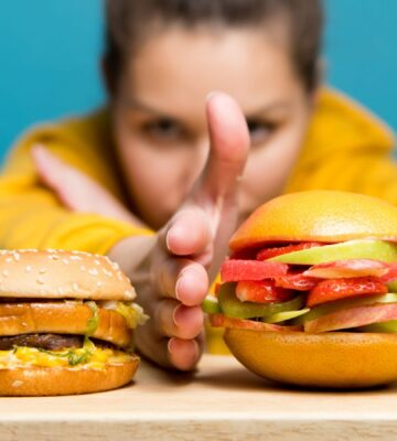 Photo shows a woman holding her hand between two burgers: a traditional beef burger on the left, and a bun filled with sliced fresh fruit on the right