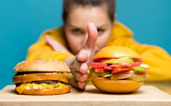 Photo shows a woman holding her hand between two burgers: a traditional beef burger on the left, and a bun filled with sliced fresh fruit on the right