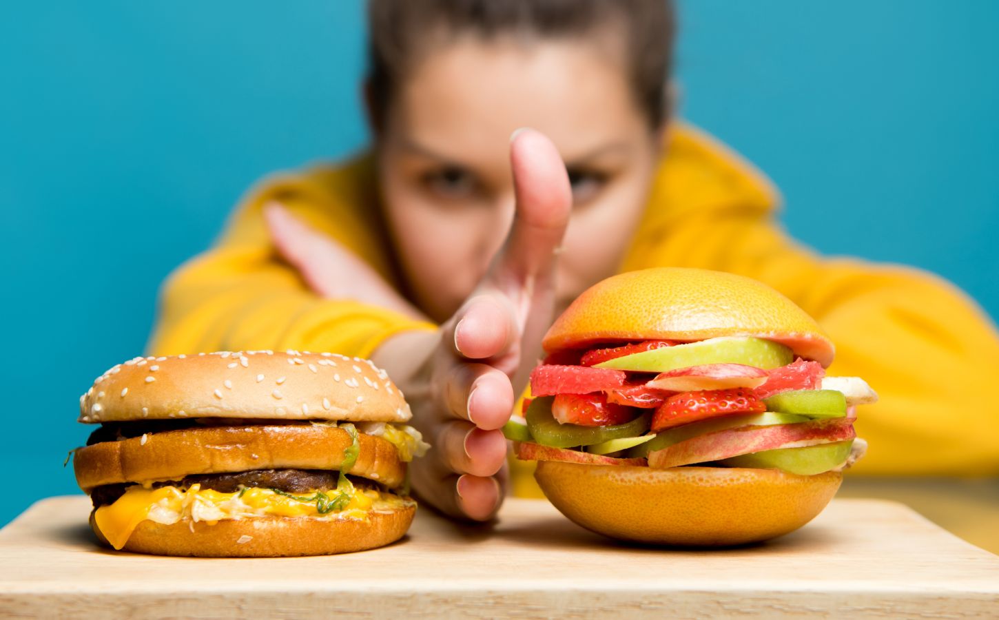 Photo shows a woman holding her hand between two burgers: a traditional beef burger on the left, and a bun filled with sliced fresh fruit on the right