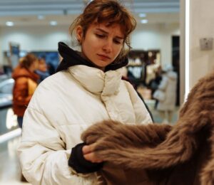Photo shows a young woman looking at a fur coat in a department store. Rick Owens just became the latest luxury fashion brand to implement a fur ban