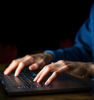 Photo shows a man typing on a brightly lit laptop and keyboard in a dark room. A whistleblower has claimed that the meat industry paid them to discredit veganism online.