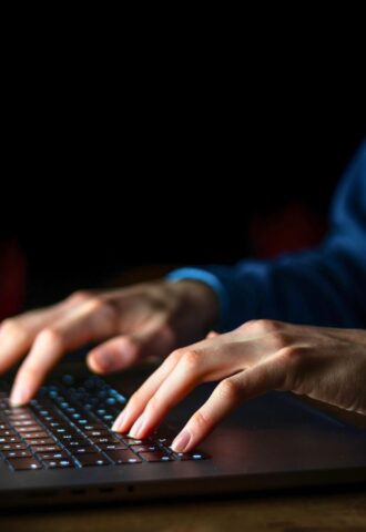Photo shows a man typing on a brightly lit laptop and keyboard in a dark room. A whistleblower has claimed that the meat industry paid them to discredit veganism online.