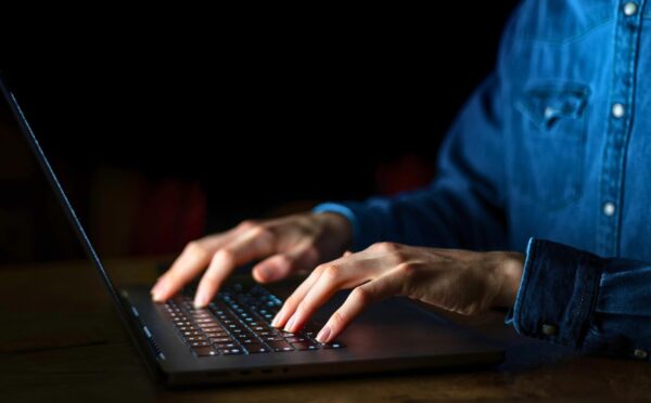 Photo shows a man typing on a brightly lit laptop and keyboard in a dark room. A whistleblower has claimed that the meat industry paid them to discredit veganism online.