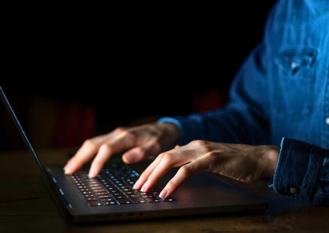 Photo shows a man typing on a brightly lit laptop and keyboard in a dark room. A whistleblower has claimed that the meat industry paid them to discredit veganism online.