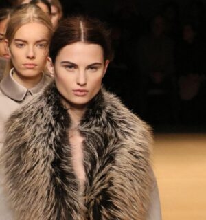 Photo shows a group of models waiting to cross the stage at a fashion event, including one model wearing a large fur coat. New York Fashion Week just announced a fur ban at all events from September 2026