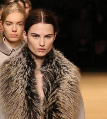 Photo shows a group of models waiting to cross the stage at a fashion event, including one model wearing a large fur coat. New York Fashion Week just announced a fur ban at all events from September 2026