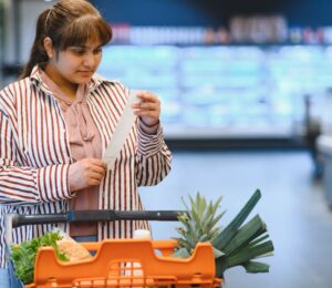 Photo shows a women reading a shopping list while pushing a trolley full of fruit and vegetables around a supermarket. A PCRM dietician says he can cut the cost of people's main holiday meal by half, provided they try a plant-based Christmas dinner
